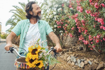 Foto de Hombre maduro disfrutar de la actividad de ocio al aire libre montar una bicicleta sola y sonriendo plantas y flores en la calle. Vida sana y feliz hombres. Concepto de transporte ecológico - Imagen libre de derechos