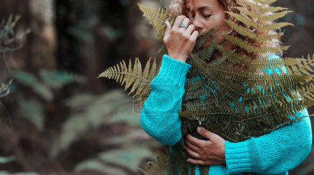 Foto de Medio ambiente y amor por la naturaleza gente concepto de estilo de vida. mujer abrazando hojas con madera verde en el fondo. Actividad de ocio al aire libre. Retrato de dama con gran hoja tropical. Conexiones - Imagen libre de derechos