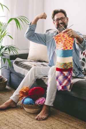 Photo for Happy man at home celebrate success after done in knitting work a piece of colorful wool using needles. Male people celebration for female hobby usual leisure activity to relax and enjoy time at home - Royalty Free Image