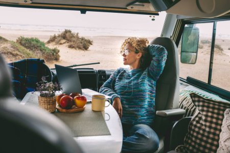 Photo for Living and working inside camper van vehicle in travel and digital nomad free lifestyle.  woman sitting in a motor home and enjoy relax and laptop connection. Beach in background outside the window - Royalty Free Image
