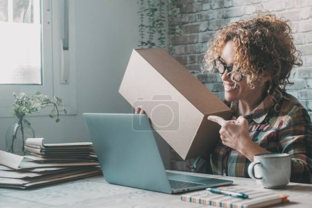 Photo for Happy woman working at office with laptop and online connection to video call buyer and showing box parcel to ship. Concept of new job business opportunity. New normal, smart working. Little company - Royalty Free Image