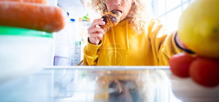 Photo for Banner of people taking food from fridge. Unhealthy food disorder lifestyle. Bad habits and dieting concept. Woman eating chocolate croissant and search for some other food to eat. Emotional eating - Royalty Free Image