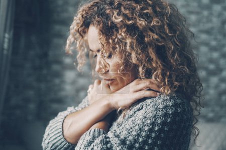Photo for Woman hugging herself to protect and love. Concept of depression and bad mental health. One female at home indoor with closed eyes. Long curly hair. Eyes closed. Interior balance wellbeing. Sadness. - Royalty Free Image