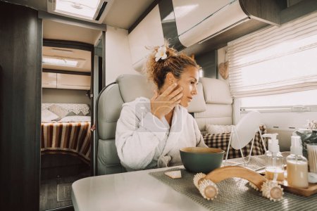 Photo for Woman having body skin care daily routine using products treatment on her face after a shower sitting inside her traveler lifestyle camper van motor home. Female people and wellness indoor leisure - Royalty Free Image