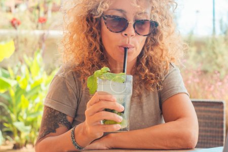 Photo for Close up portrait of  woman drinking mojito fresh cocktail at the beach bar cafe. Tourist enjoying leisure and summer vacation lifestyle. People with beverage. Modern trendy female tattoo - Royalty Free Image