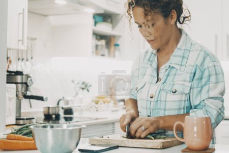 Photo for Close up portrait or real life scene with one single woman at home cutting vegetables to prepare diet healthy lunch alone at home. White kitchen in background. People  and health food. Lady at work - Royalty Free Image