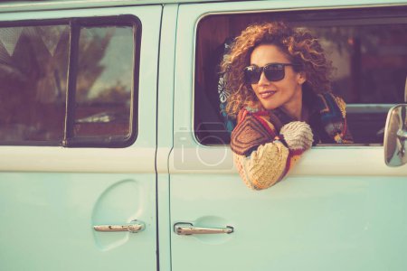 Photo for Retro classic travel vehicle and people concept.  Beautiful adult woman inside a blue van. Transport vehicle and freedom. Alternative lifestyle lady with curly hair. Cheerful female traveler smile - Royalty Free Image