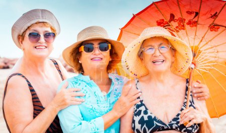 Photo for Group of women people pose for a picture in summer. Senior aged ladies smile and enjoy holiday vacation with beach style and lifestyle. Older females smiling under the sun wearing colors accessories - Royalty Free Image