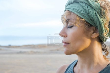 Photo for Middle age pretty woman outdoor with closed eyes and serene expression and nature outdoor beach in background. Concept of wellbeing and mindful relax. Enjoying outdoors calm leisure activity alone - Royalty Free Image