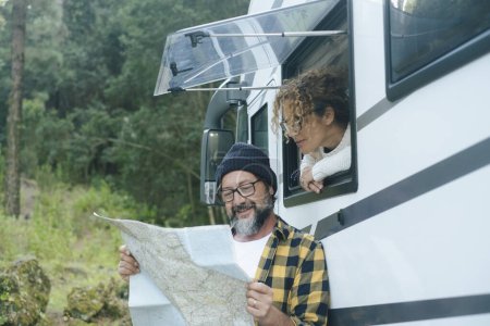  happy traveler couple looking together a paper guide map to choose plan next travel destination. Living in a van. Nomadic people, Vanlife. Alternative vehicle vacation journey. Road trip planning