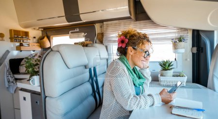 Photo for Solo traveler woman enjoy time and indoor leisure activity inside a modern camper van motorhome using mobile phone and roaming wireless connection. Modern people and technology on travel concept - Royalty Free Image