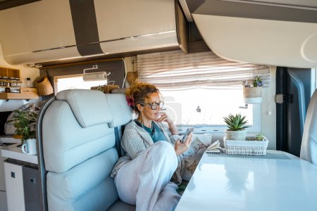 Photo for Adult woman relaxing inside a modern luxury camper van rv vehicle motorhome reading notification on cell phone. Alternative home vanlife style and tourism renting van. Tiny house. Traveler lifestyle - Royalty Free Image