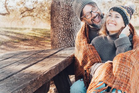 Téléchargez les photos : Couple adulte s'amuser ensemble avec amour et rire assis ensemble sur un banc dans le parc de la saison d'automne. Les gens aiment les loisirs de plein air et rient. Homme embrasser femme souriant beaucoup. Relation - en image libre de droit