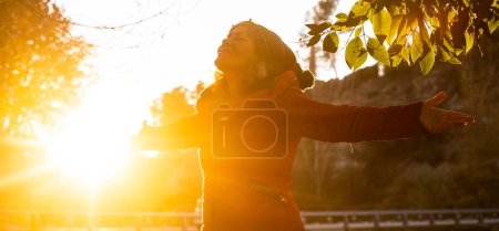 Photo for Autumn outdoor leisure activity people.  woman outstretching arms at the park against a golden sunset. Female and happiness. Freedom in nature. Overjoyed lady opening arms and smile. Wellbeing. - Royalty Free Image