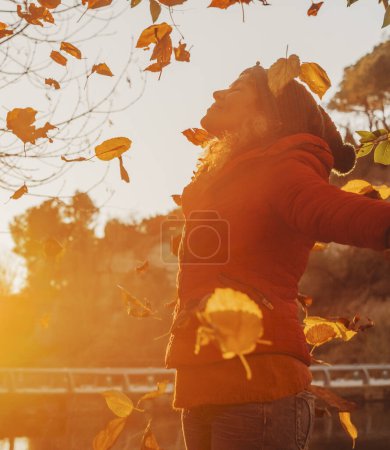 Photo for Winter is coming. Autumn sunset and happy woman throwing leaves in the air, opening arms and smiling with happiness. Serene wellbeing people and natural healthy lifestyle. Outdoor leisure activity lady - Royalty Free Image