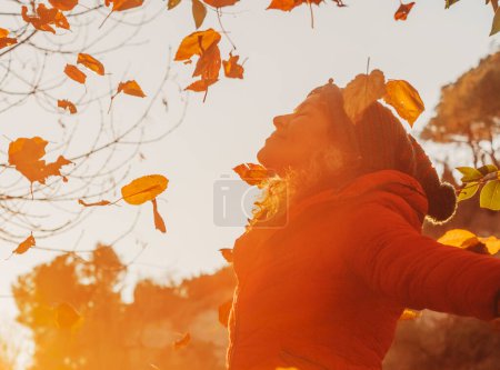 Téléchargez les photos : Overjoy et bonheur émotion gens. femme jetant des feuilles dans l'air au parc pendant la couleur chaude coucher de soleil rouge en automne saison. Personnes et sentiment de liberté ou de joie. J'aime la nature. Jouer en plein air - en image libre de droit