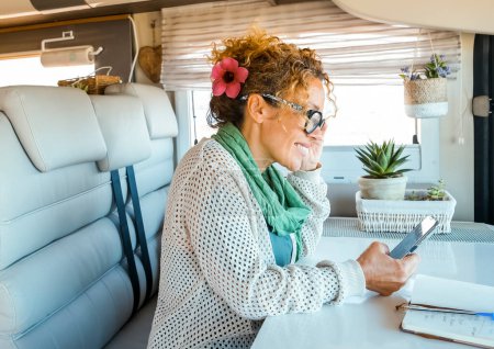 One solo traveler woman enjoy time and indoor leisure activity inside a modern camper van motor home using mobile phone and roaming wireless connection. Modern people and technology on travel concept