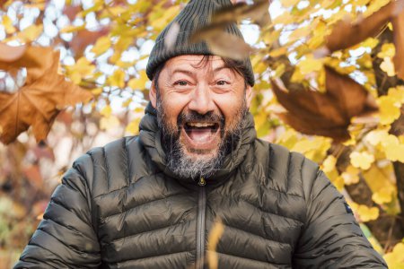 Téléchargez les photos : Portrait d'homme à l'expression réjouie dans les activités de loisirs de plein air en automne avec des feuilles orange et jaune fond de nature. Bonheur et joyeux hommes avec des vêtements verts à l'extérieur - en image libre de droit
