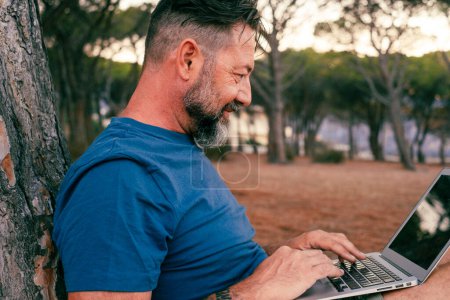 Photo for Adult man using and working on laptop at the park. Concept of smart working and freelance digital nomad small business online free lifestyle. People with computer outdoor leisure activity - Royalty Free Image