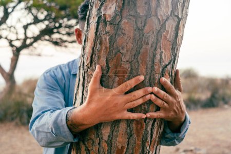 Photo for People hugging tree. Nature environment climate change and protection life. Hidden male embrace bonding a trunk at the park. Close up of hands on the wood. Touching nature in outdoor leisure activity - Royalty Free Image