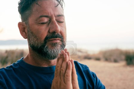 Photo for Adult man praying and meditate outdoor in relaxation gesture with hands clasped and closed eyes, portrait. Zen like healthy mental balance lifestyle, male people. Wellbeing. People zen exercise - Royalty Free Image