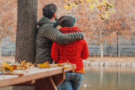 Photo for Dating couple viewed from back enjoy scenic view at the lake in autumn winter day. Love and relationship. Romantic moment for man and woman hugging and enjoying outdoor leisure activity together - Royalty Free Image