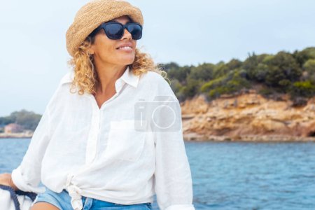Foto de Hembra adulta serena sentada en un barco disfrutando de una excursión por la costa durante las vacaciones de verano. Isla de fondo. Concepto de viaje y libertad estilo de vida de las personas en el mar - Imagen libre de derechos