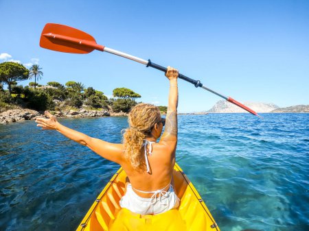 Téléchargez les photos : Vue arrière d'une touriste excitée à l'intérieur d'un canoë-kayak avec le littoral et les îles en arrière-plan profiter et s'amuser pendant les vacances d'été Voyage. Heureux tourisme des gens. Loisirs de plein air dame - en image libre de droit