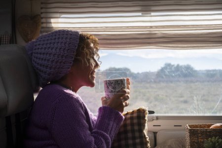 Photo for Woman side view smile and enjoy travel lifestyle and destination drinking coffee and admiring the view outside the widow of her camper van. Van life. Alternative vehicle travel vacation people - Royalty Free Image
