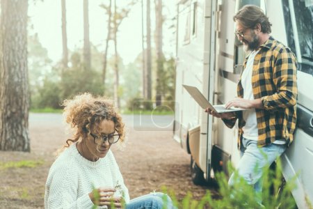 Photo for Travel couple adult people man and woman enjoy outdoor leisure activity outside a modern rv vehicle camper van parking in the forest. Adventure traveler vanlife lifestyle. Digital nomad using computer - Royalty Free Image