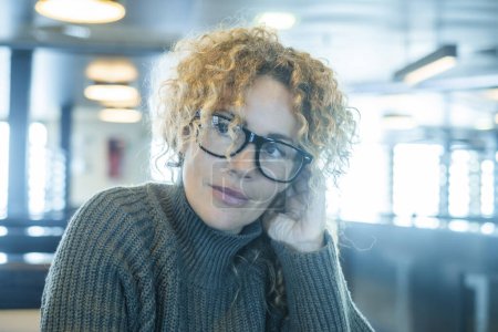 Photo for Portrait of cute pretty woman smiling indoor inside cafe bar wearing glasses. Middle age beauty female people with curly hair. Serene expression person in interior leisure relax activity alone - Royalty Free Image