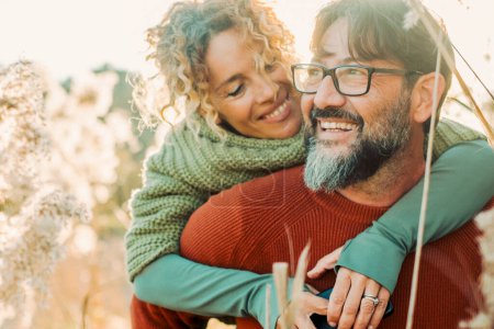 Photo for Happy couple enjoy outdoor leisure activity together, having fun and love in relationship and friendship. adult man carrying woman in piggyback in a golden field in sunset light. Mature lifestyle - Royalty Free Image
