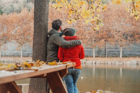Photo for Dating couple viewed from back enjoy scenic view at the lake in autumn winter day. Love and relationship. Romantic moment for man and woman hugging and enjoying outdoor leisure activity together - Royalty Free Image