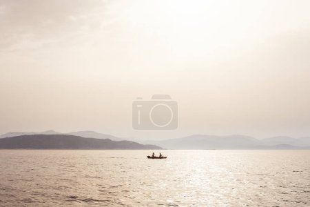 Photo for Misty mood seascape with fishermen boat in the middle of the sea and coastline in background under fog sunlight. - Royalty Free Image