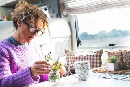 Photo for Woman caring plants and flowers inside a camper van modern tiny house motorhome rv alone. People living van life full time. People and nature. Happy young mature female indoor leisure - Royalty Free Image