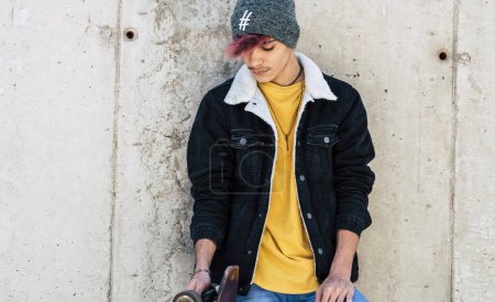 Photo for Standing young boy portrait with casual clothes trendy fashion style against a urban wall with skate board. Concept of youth teen lifestyle. Modern generation people posing for picture. Model. - Royalty Free Image
