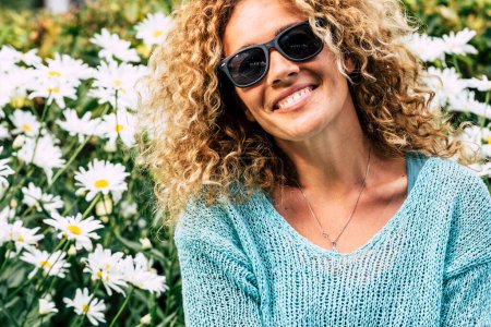 Photo for Portrait of joyful beautiful adult woman with curly hair and sunglasses and garden park daisies flowers background Concept of people and leisure activity in spring season. Copy space on left - Royalty Free Image