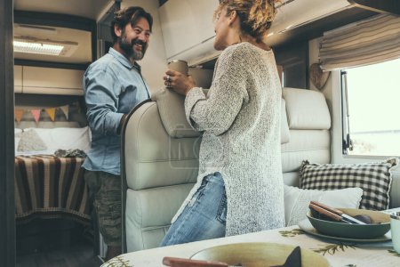 Photo for Happy adult couple enjoy vacation on camper van and prepare lunch together. Alternative travel lifestyle for modern people. Man and woman smile inside motor home. Van life and holiday trip vacation - Royalty Free Image