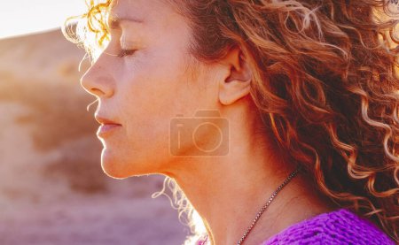 Photo for Close up sunset portrait of attractive woman with closed eyes and sun in backlight. Dreaming and enjoying feeling concept lifestyle emotion. Serene female people outdoor with curly hair - Royalty Free Image