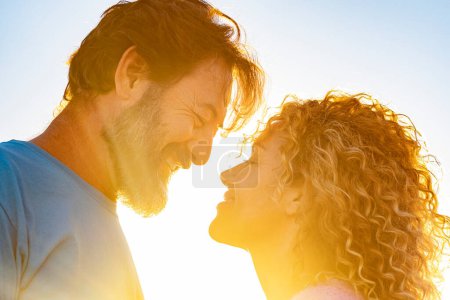 Téléchargez les photos : Couple heureux adulte en amour et relation plus proche face à face contre un coucher de soleil avec des couleurs dorées. Homme et femme profiter de l'amour en plein air avec ciel bleu en arrière-plan et l'espace de copie - en image libre de droit