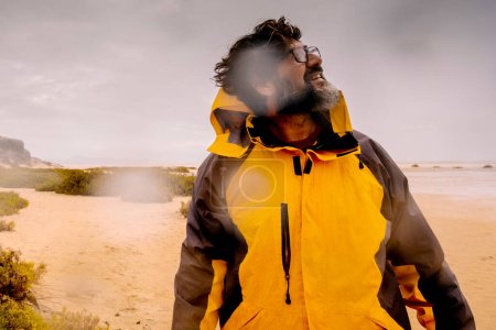 Photo for Standing explorer adventure man walking down the rain at the beach. Concept of bad weather nature and feeling. Male people with yellow jacket in outdoor leisure activity - Royalty Free Image