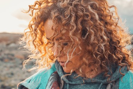 Téléchargez les photos : Side portrait of attractive woman with blonde colored long curly hair looking down and enjoying outdoors nature feeling. Travel adult female people concept lifestyle with desert in background - en image libre de droit