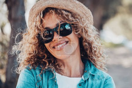 Téléchargez les photos : Portrait de femme adulte souriant à la caméra avec des lunettes de soleil et un chapeau de paille. Les femmes heureux dans l'activité de loisirs de plein air. Fond déconcentré avec la route. Copier l'espace sur la droite - en image libre de droit