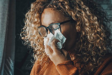 Foto de Woman sneezing nose with fever and influenza virus health disease. Flu and cold for winter temperature at home. People suffering for unhealthy bad condition indoor. Female with paper towels - Imagen libre de derechos