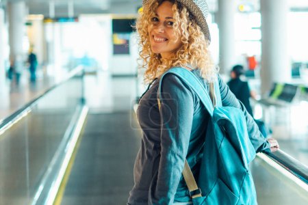 Téléchargez les photos : Femme adulte gaie voyage à l'aéroport avec sac à dos. Portrait de femmes souriantes et marchant à la porte. Jolie dame blonde voyageur profiter du voyage et vacances loisirs activité - en image libre de droit