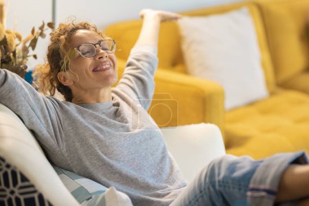Foto de Feliz mujer caucásica adulta sentada en una silla en casa en la sala de estar abre los brazos y sonríe mucho. Éxito y satisfacción estilo de vida las mujeres han relajado la actividad de ocio - Imagen libre de derechos