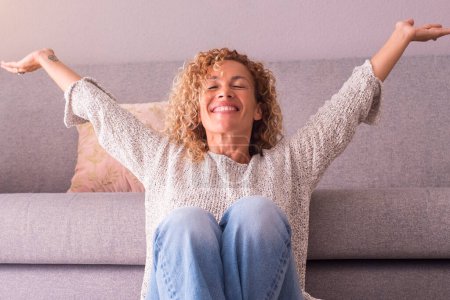 Photo for Happy and satisfied woman at home sitting on the floor opening arms and smiling. Concept of joyful lifestyle, female people. Indoor leisure activity, Success and enjoying lifestyle. Indoor apartment - Royalty Free Image