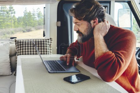 Photo for Modern adult man work on laptop computer in remote working and digital job lifestyle inside a modern and connected camper van with nature woods view outside the window. Freedom lifestyle people - Royalty Free Image