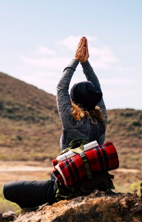 Foto de Vista posterior de la mujer aventura haciendo yoga posición saludable frente a una montaña en la actividad de trekking al aire libre solo. Senderismo y meditación zen concepto de estilo de vida. Mujeres viajan alternativa - Imagen libre de derechos