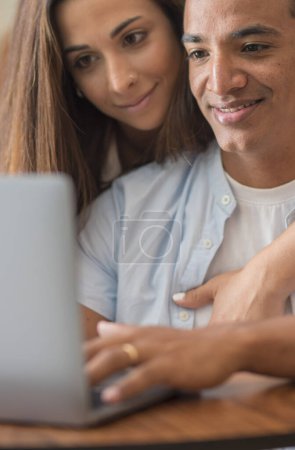 Photo for Couple using together a laptop at home sitting and enjoying the web. Young couple interracial people working on computer and smiling. People and technology. Man and woman use notebook online - Royalty Free Image